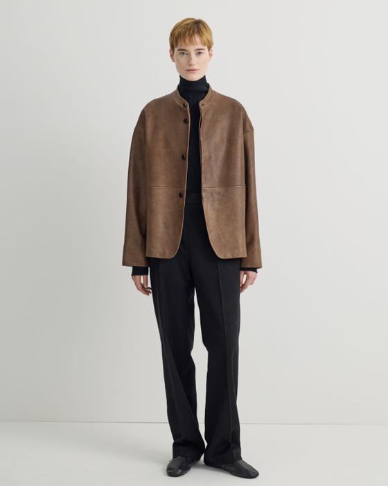 A woman wearing a brown suede Taiga Takahashi jacket with a black turtleneck and black trousers