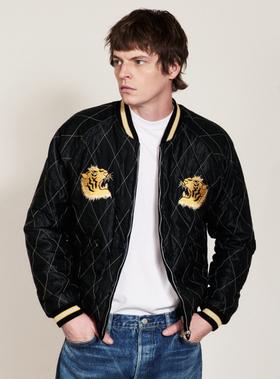 A man wearing a black quilted Tailor Toyo souvenir jacket with embroidered tiger heads over a white tee
