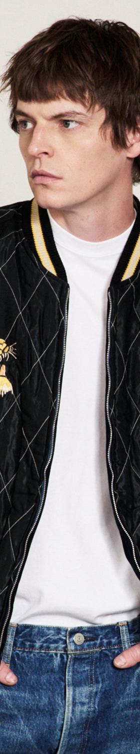 A man wearing a black quilted Tailor Toyo souvenir jacket with embroidered tiger heads over a white tee