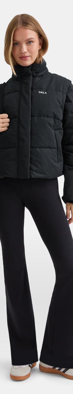 A woman wearing a black TALA puffer jacket with black flared leggings