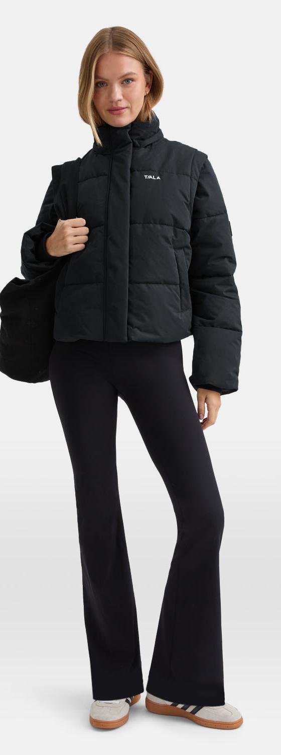 A woman wearing a black TALA puffer jacket with black flared leggings