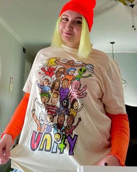 A woman wearing a cream Teen Hearts graphic t-shirt with orange layered sleeves and a red beanie