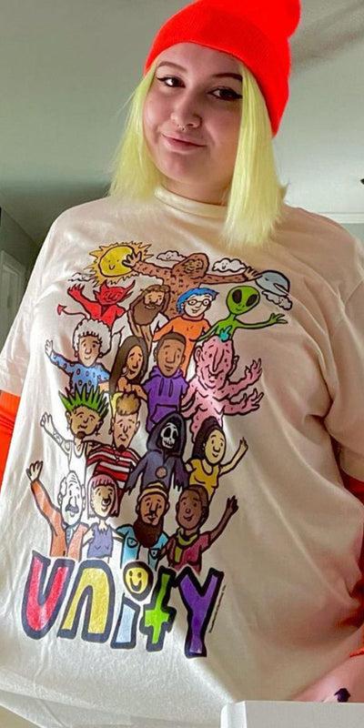 A woman wearing a cream Teen Hearts graphic t-shirt with orange layered sleeves and a red beanie