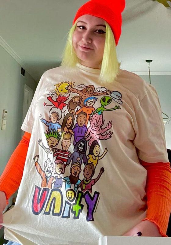 A woman wearing a cream Teen Hearts graphic t-shirt with orange layered sleeves and a red beanie