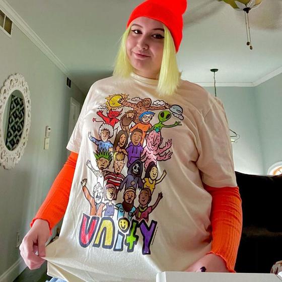 A woman wearing a cream Teen Hearts graphic t-shirt with orange layered sleeves and a red beanie
