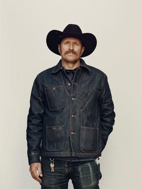 A man in a black cowboy hat wearing a raw indigo Tellason denim chore jacket and jeans