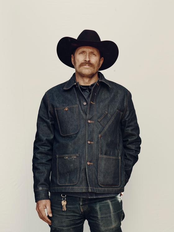 A man in a black cowboy hat wearing a raw indigo Tellason denim chore jacket and jeans