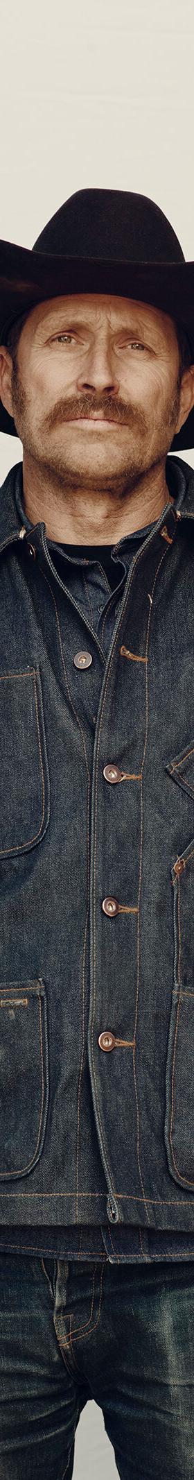 A man in a black cowboy hat wearing a raw indigo Tellason denim chore jacket and jeans