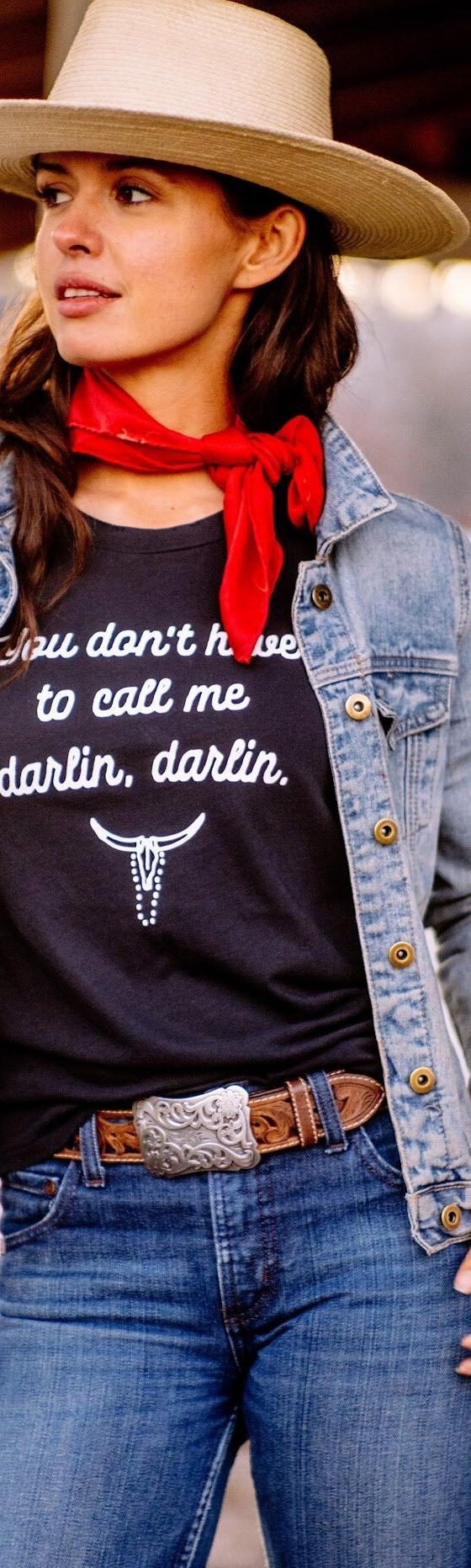 A woman wearing a straw wide-brim hat, denim jacket and red neckerchief with a black The Salt Ranch tee