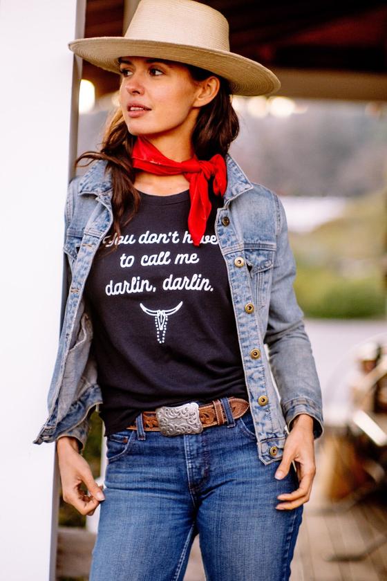 A woman wearing a straw wide-brim hat, denim jacket and red neckerchief with a black The Salt Ranch tee