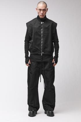 A man wearing a black thom/krom bomber jacket with layered vest and wide drop-crotch trousers