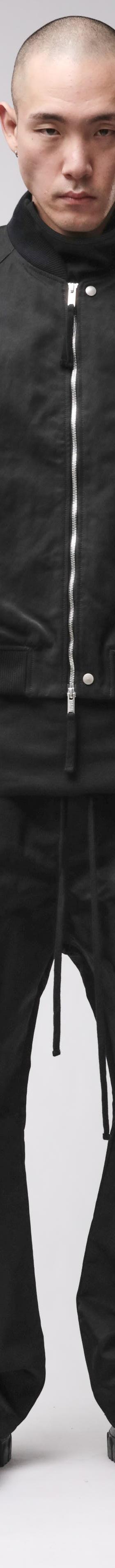 A man wearing a black thom/krom bomber jacket with layered vest and wide drop-crotch trousers