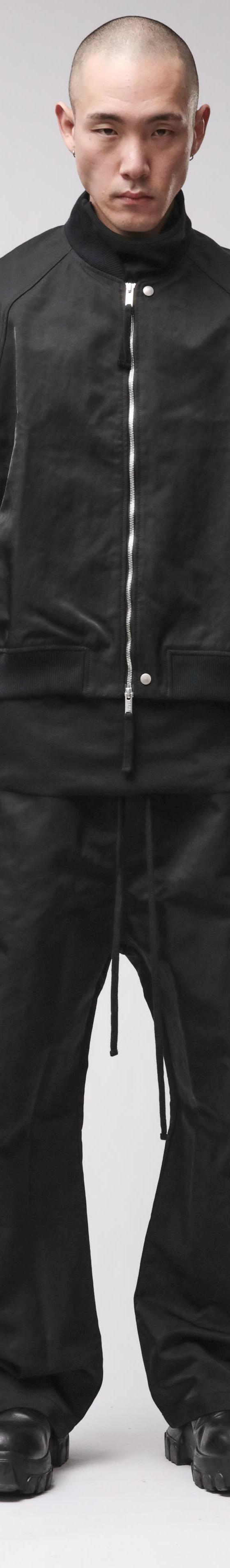 A man wearing a black thom/krom bomber jacket with layered vest and wide drop-crotch trousers