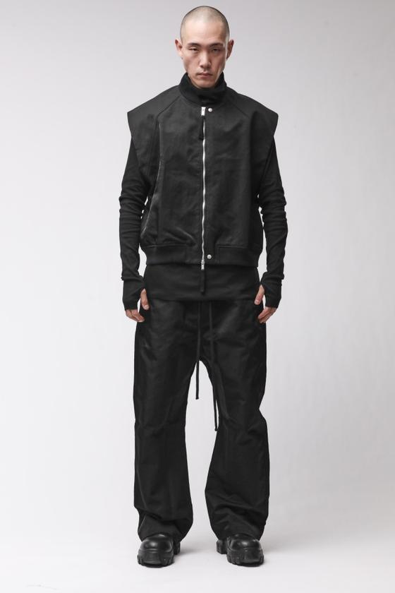 A man wearing a black thom/krom bomber jacket with layered vest and wide drop-crotch trousers