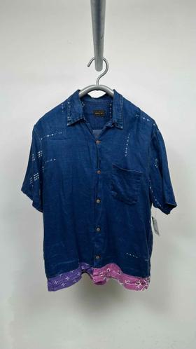 An indigo denim short-sleeve camp collar shirt with pink bandana patchwork hem, photographed on a hanger against a grey wall