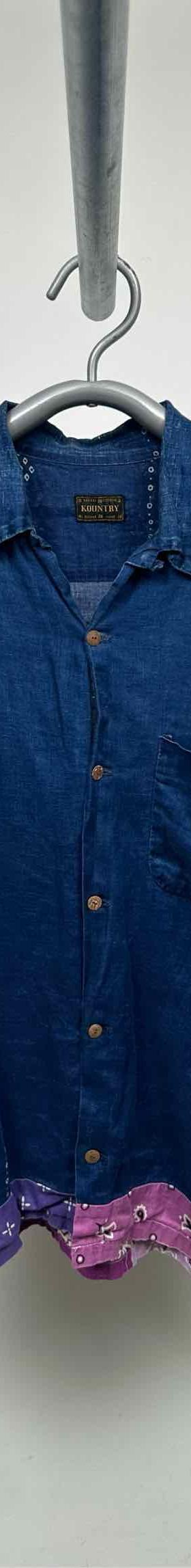 An indigo denim short-sleeve camp collar shirt with pink bandana patchwork hem, photographed on a hanger against a grey wall