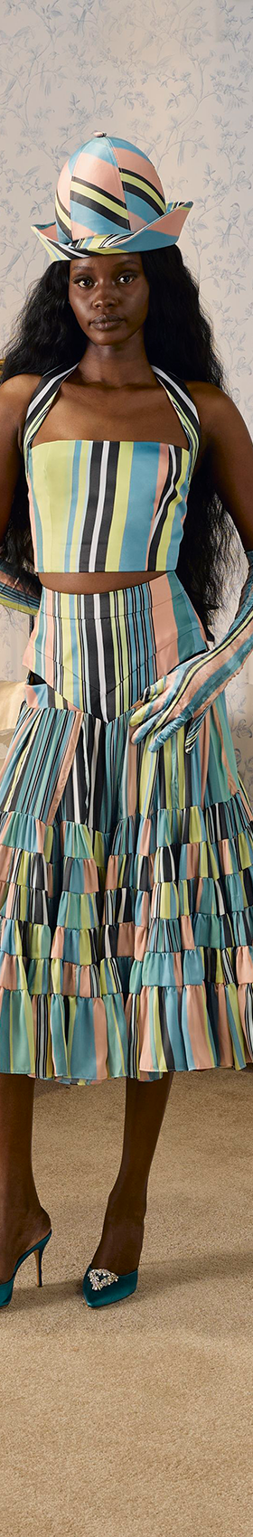 A woman wearing a striped pleated Tolu Coker skirt set with matching hat and gloves