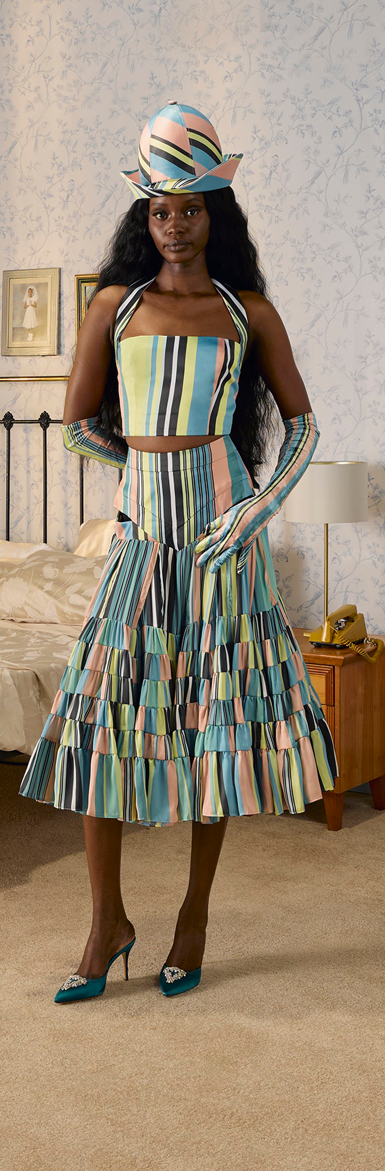 A woman wearing a striped pleated Tolu Coker skirt set with matching hat and gloves