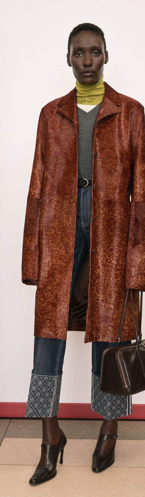 A woman wearing a brown printed leather coat with a leather belt and carrying a dark brown leather doctor's bag