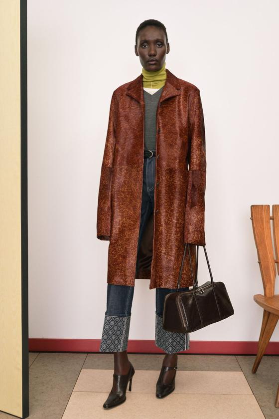 A woman wearing a brown printed leather coat with a leather belt and carrying a dark brown leather doctor's bag