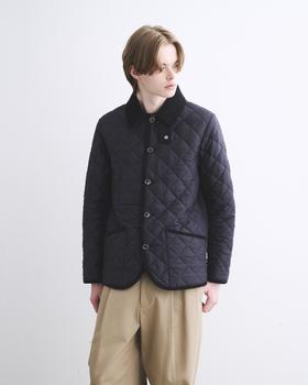 A man wearing a navy quilted Traditional Weatherwear jacket with corduroy collar and beige trousers