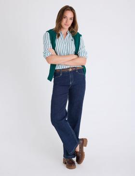 A woman wearing a U.S. Polo Assn. striped shirt with a green cable-knit sweater and dark jeans