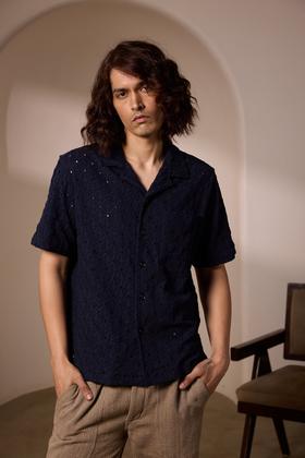 A man wearing a navy textured camp-collar shirt and beige linen trousers