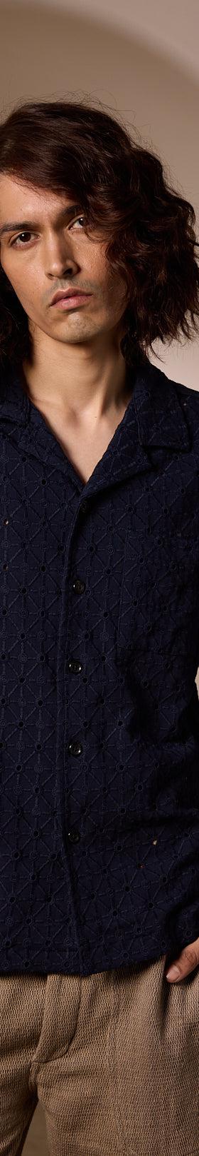 A man wearing a navy textured camp-collar shirt and beige linen trousers