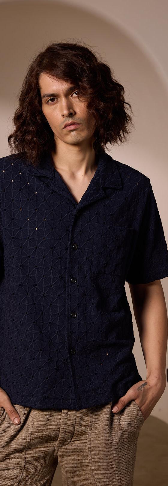 A man wearing a navy textured camp-collar shirt and beige linen trousers