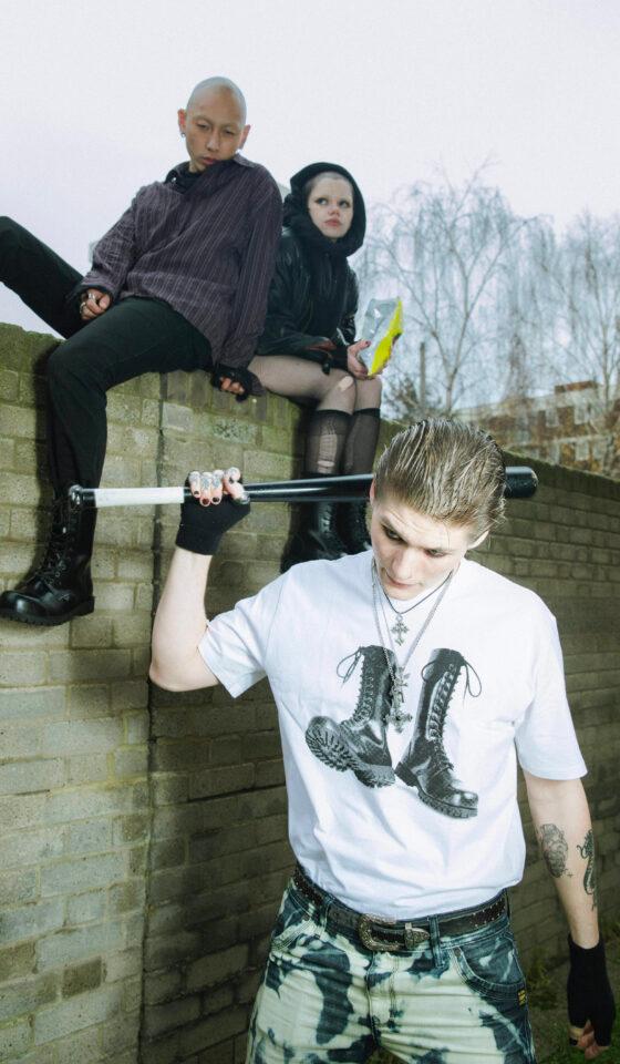 Three people in punk streetwear and black lace-up Underground England boots on a brick wall