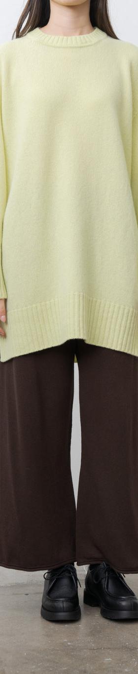 A woman wearing an oversized pale yellow unfil knit sweater with wide brown trousers