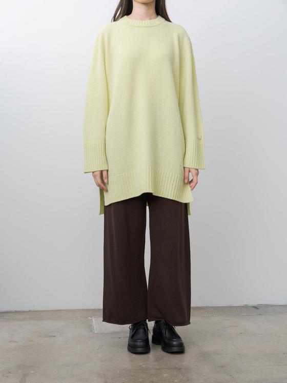 A woman wearing an oversized pale yellow unfil knit sweater with wide brown trousers