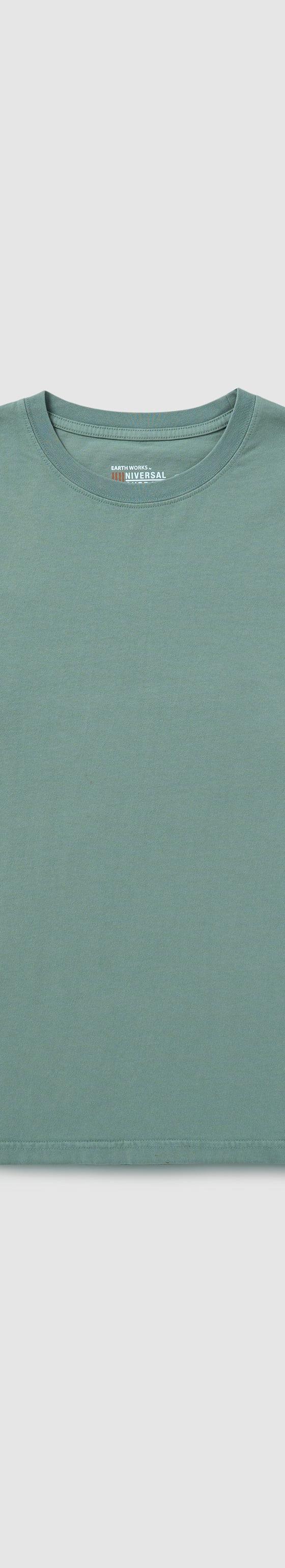 A sage green UNIVERSAL OVERALL long-sleeve cotton tee laid on a plain grey background