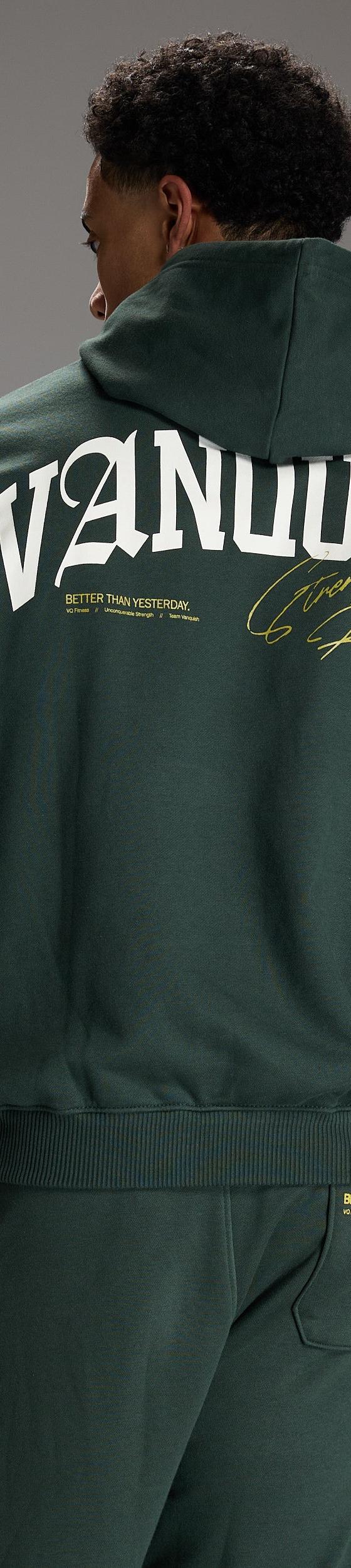 A man wearing a dark green Vanquish Fitness hoodie and matching joggers, shot from behind