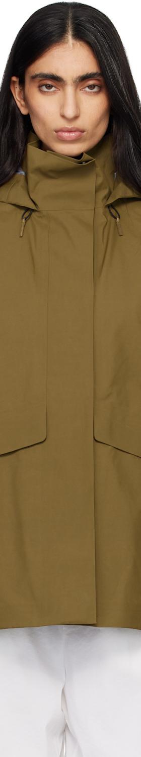 A woman wearing a khaki Veilance hooded technical jacket with white trousers