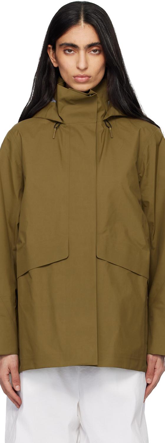 A woman wearing a khaki Veilance hooded technical jacket with white trousers