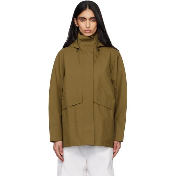 A woman wearing a khaki Veilance hooded technical jacket with white trousers