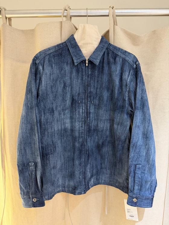 An indigo denim zip jacket hung against a linen backdrop