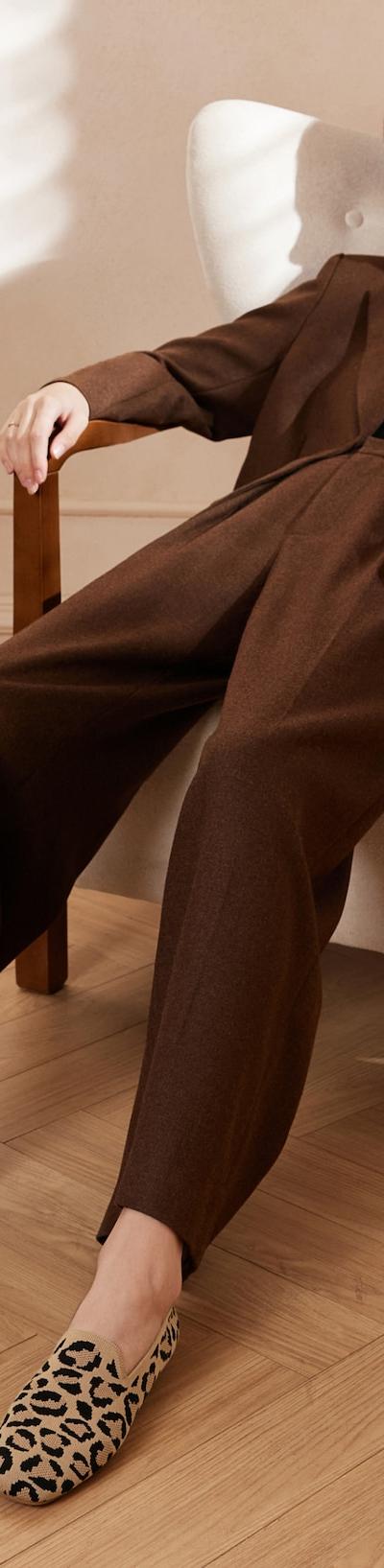 A woman in a brown suit seated in an armchair, wearing leopard-print VIVAIA knit flats