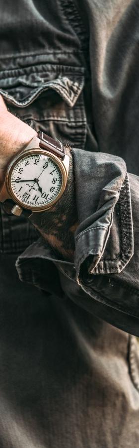 A man in a washed grey denim jacket wearing a Vortic Watch Company wristwatch with a white vintage dial and leather strap
