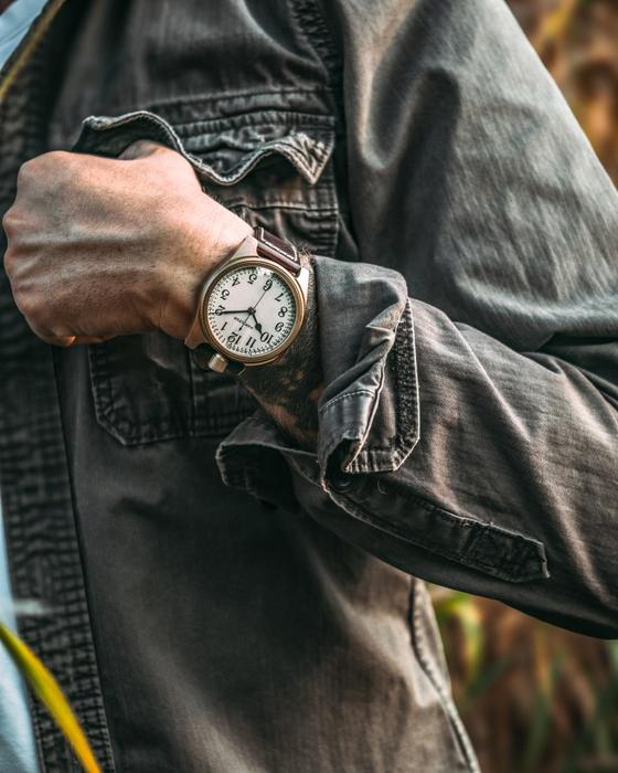 A man in a washed grey denim jacket wearing a Vortic Watch Company wristwatch with a white vintage dial and leather strap