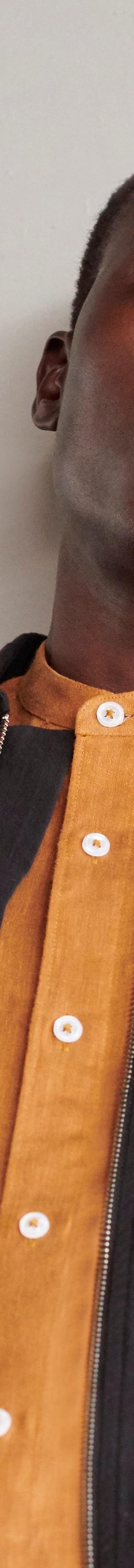 A man wearing a black cotton overshirt layered over a rust-orange button-up shirt