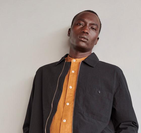A man wearing a black cotton overshirt layered over a rust-orange button-up shirt