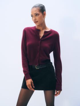 A woman wearing a burgundy White & Warren cashmere cardigan with a black suede mini skirt