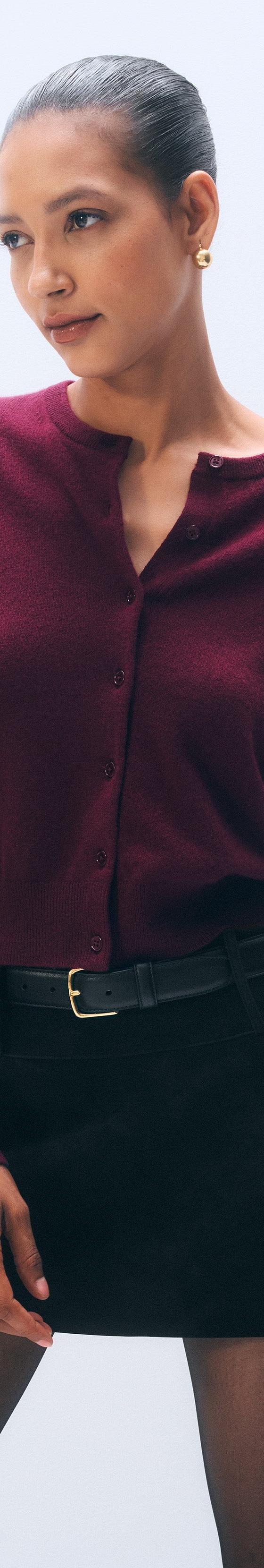 A woman wearing a burgundy White & Warren cashmere cardigan with a black suede mini skirt