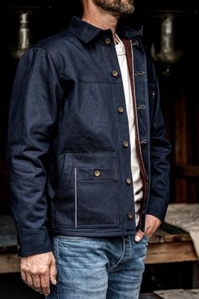 A man wearing an indigo denim chore jacket over a cream tee and faded jeans