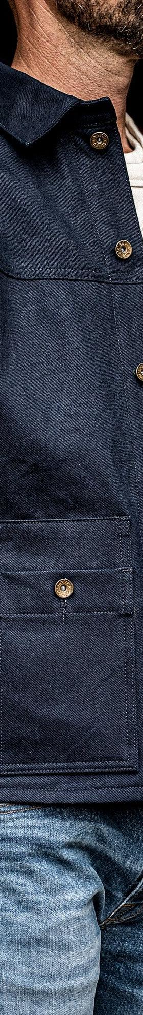 A man wearing an indigo denim chore jacket over a cream tee and faded jeans