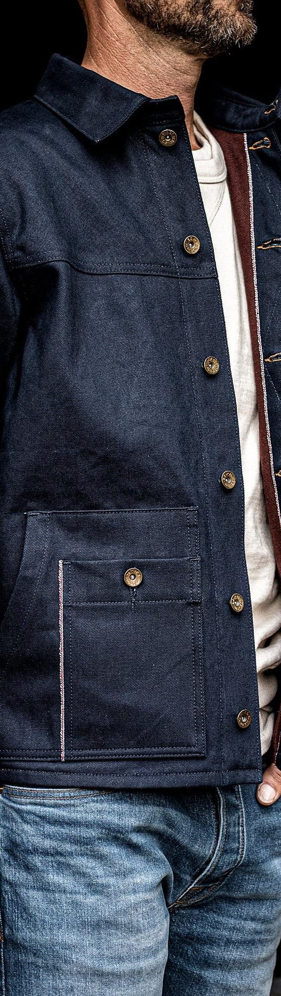 A man wearing an indigo denim chore jacket over a cream tee and faded jeans