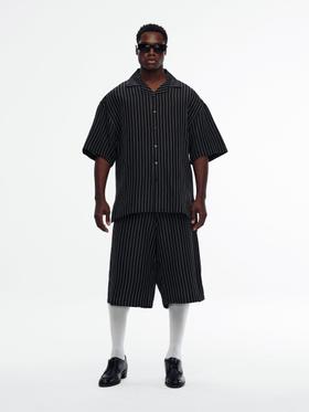 A man wearing a black pinstripe Willy Chavarria camp-collar shirt with matching wide shorts