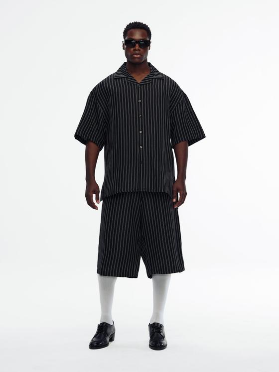 A man wearing a black pinstripe Willy Chavarria camp-collar shirt with matching wide shorts